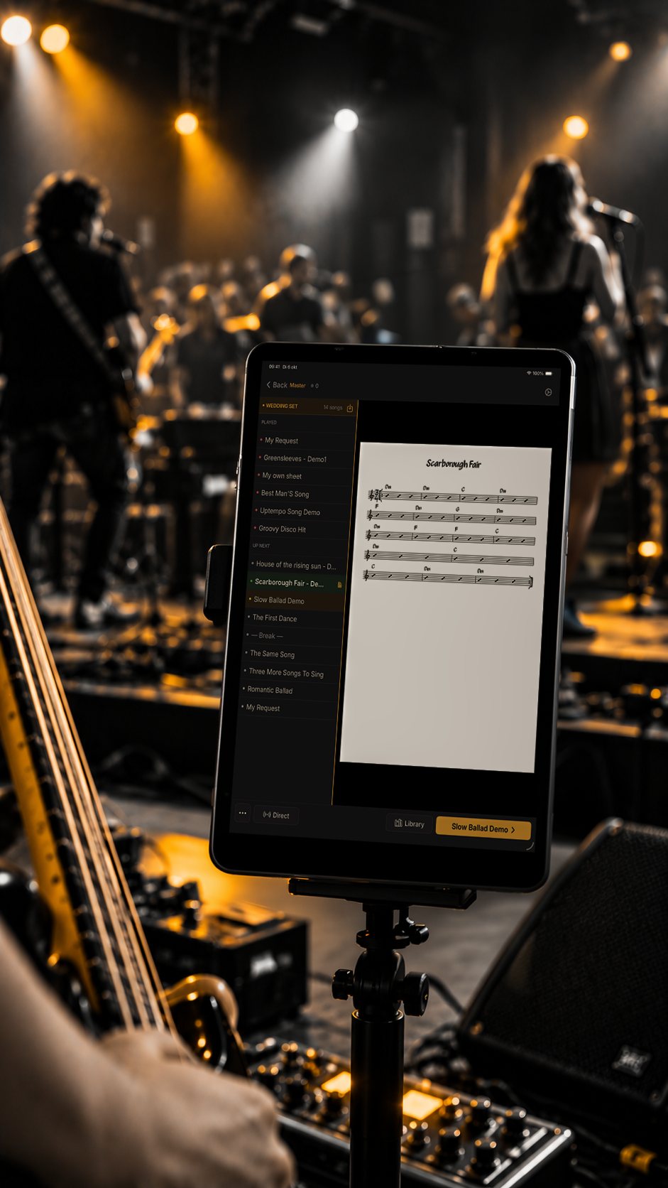 iPad on a stand on stage showing the setlist and a chart, band in amber stage light